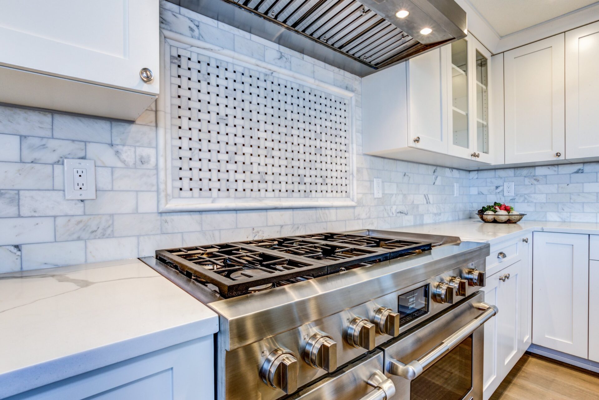 White kitchen with stainless steel hood over gas cooktop and carrera marble backsplash. white kitchen with stainless steel hood